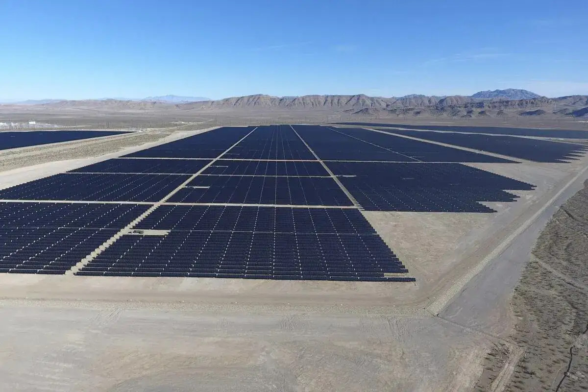 Vasto parque solar en un paisaje des&eacute;rtico, con hileras interminables de paneles oscuros bajo un cielo azul claro.