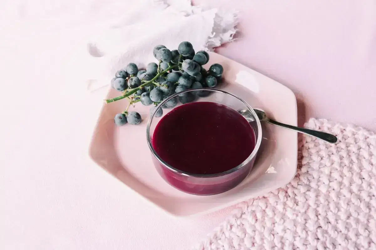 Un bicchiere di mosto cotto, denso e scuro, accanto a un grappolo d'uva nera. Una deliziosa ricetta autunnale.