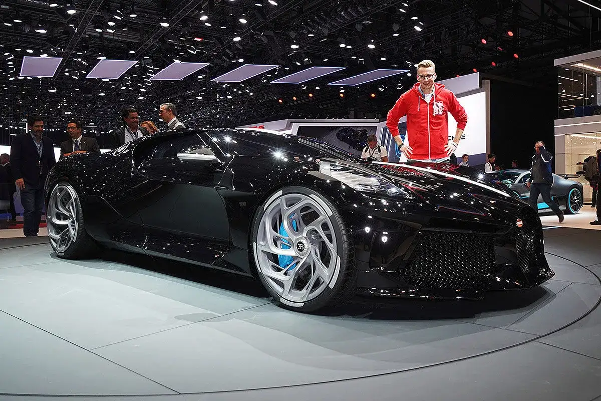 Ein Mann im roten Hoodie posiert neben dem Bugatti La Voiture Noire. Der Besitzer dieses einzigartigen Autos ist ein echter Kenner.