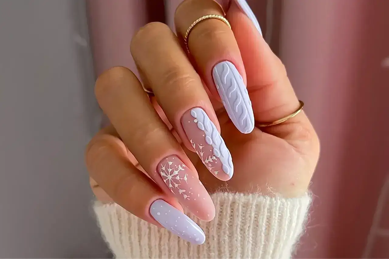 Manucure hivernale parfaite pour janvier : ongles longs avec motifs de tricot blanc, flocons de neige et pois discrets sur fond pastel.