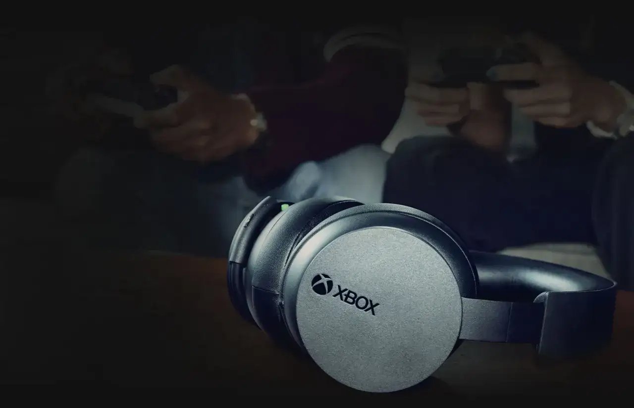 Słuchawki Xbox na pierwszym planie, w tle gracze z kontrolerami. Idealne, gdy zastanawiasz się, jakie słuchawki do Xbox Series X wybrać.
