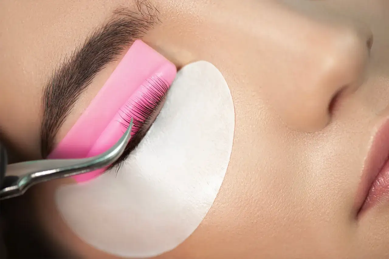 Application d'un soin pour l'allongement des cils, avec une pince et un coussinet protecteur.