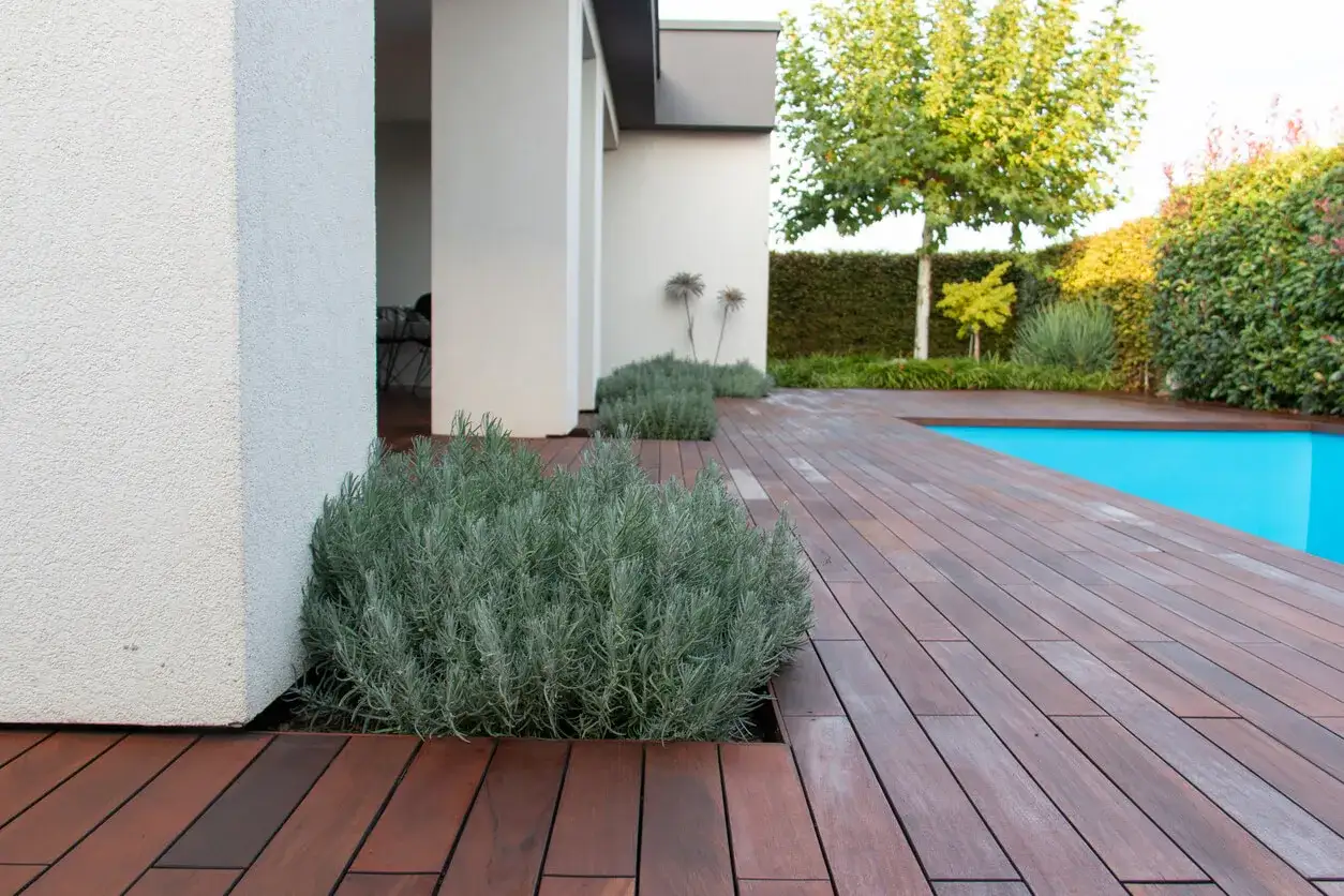 Terraza de madera con tratamiento para exterior, junto a piscina y vegetaci&oacute;n.
