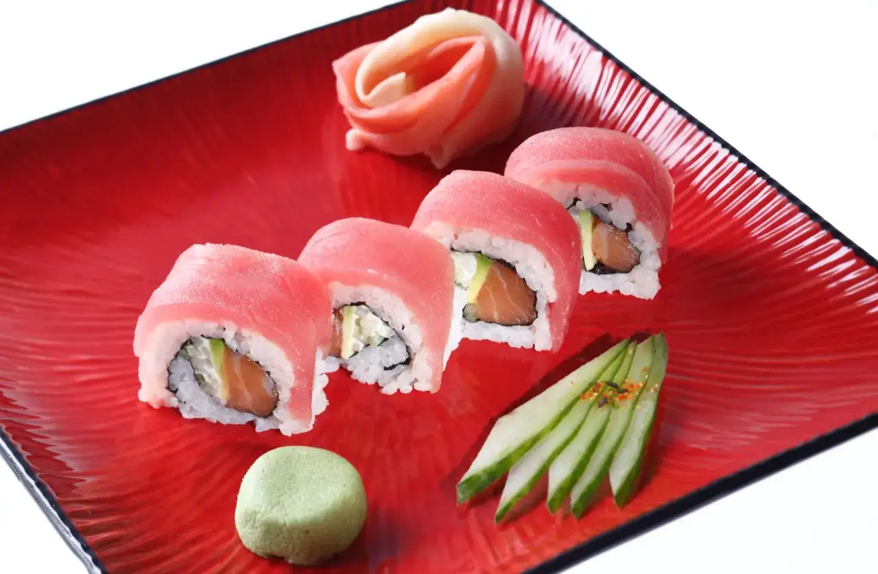Roladki sushi z łososiem i awokado na czerwonym talerzu. Obok wasabi, marynowany imbir i plasterki ogórka. Idealne na letnie dni, gdy zastanawiasz się, jaka sałata do sushi będzie najlepsza.