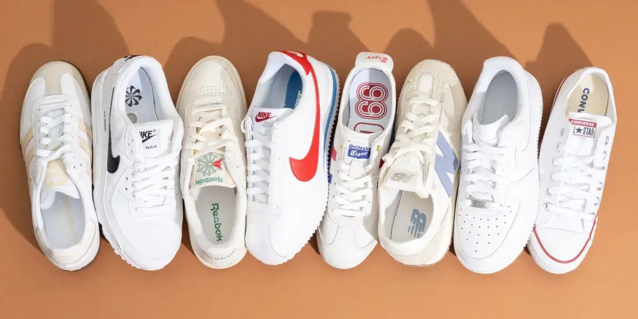 Una fila di sneakers bianche di varie marche: Adidas, Nike, Reebok, Onitsuka Tiger, New Balance, Converse. Il loro significato è stile e comfort.