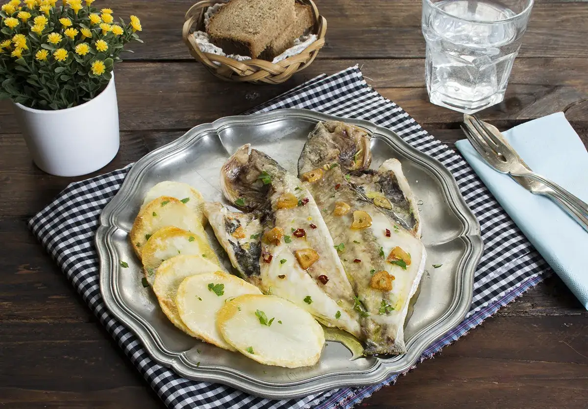Dorada a la espalda, servida con patatas panadera y decorada con ajo y perejil. Un plato sencillo y delicioso.
