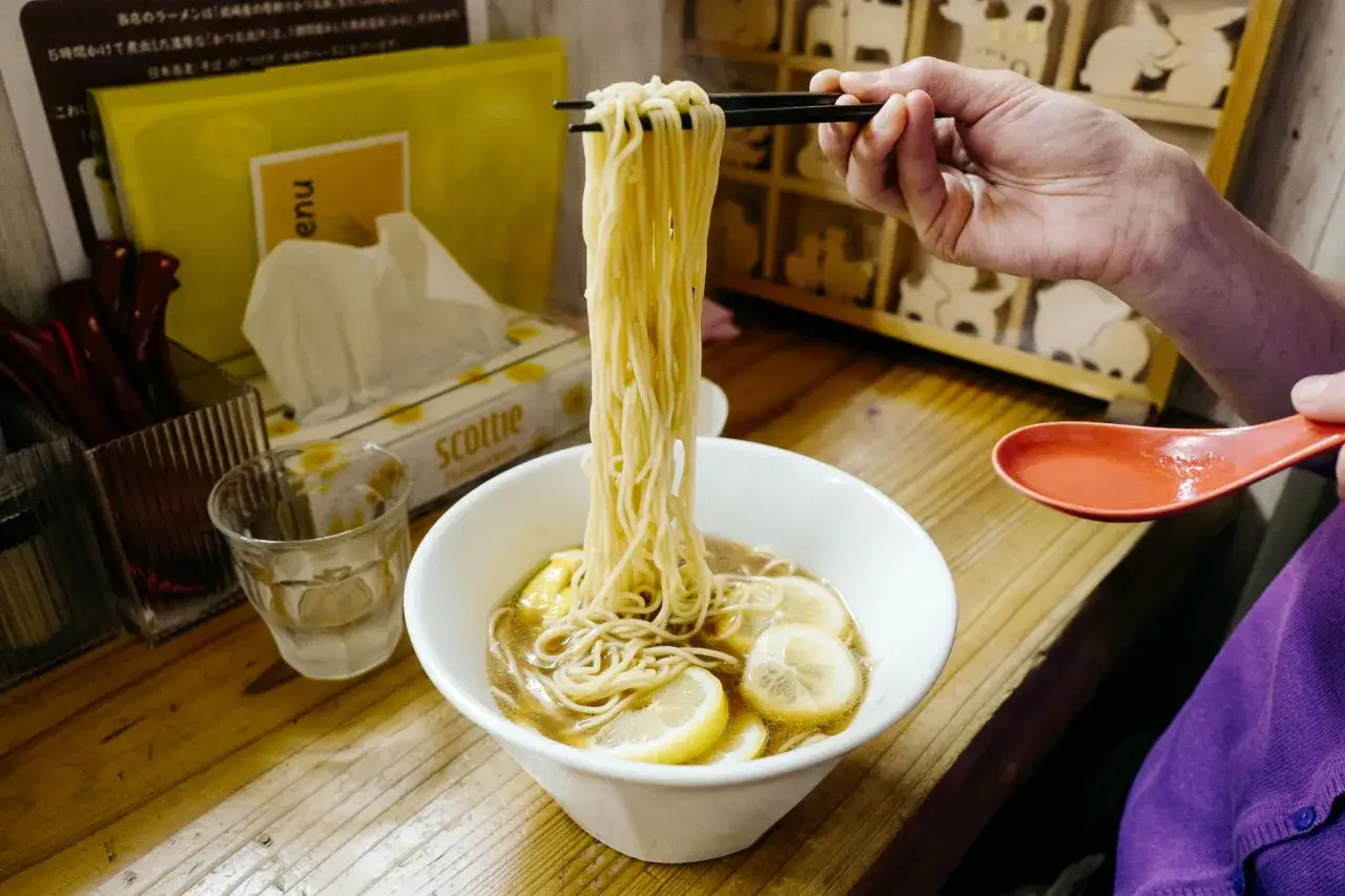Chwytam pałeczkami porcję cienkiego makaronu z miski z bulionem i plasterkami cytryny. Czy to ramen, czy udon?