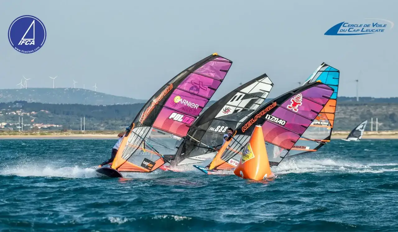 Windsurfer Maciej Rutkowski kämpft sich durch die Wellen, seine Segel in leuchtenden Farben.