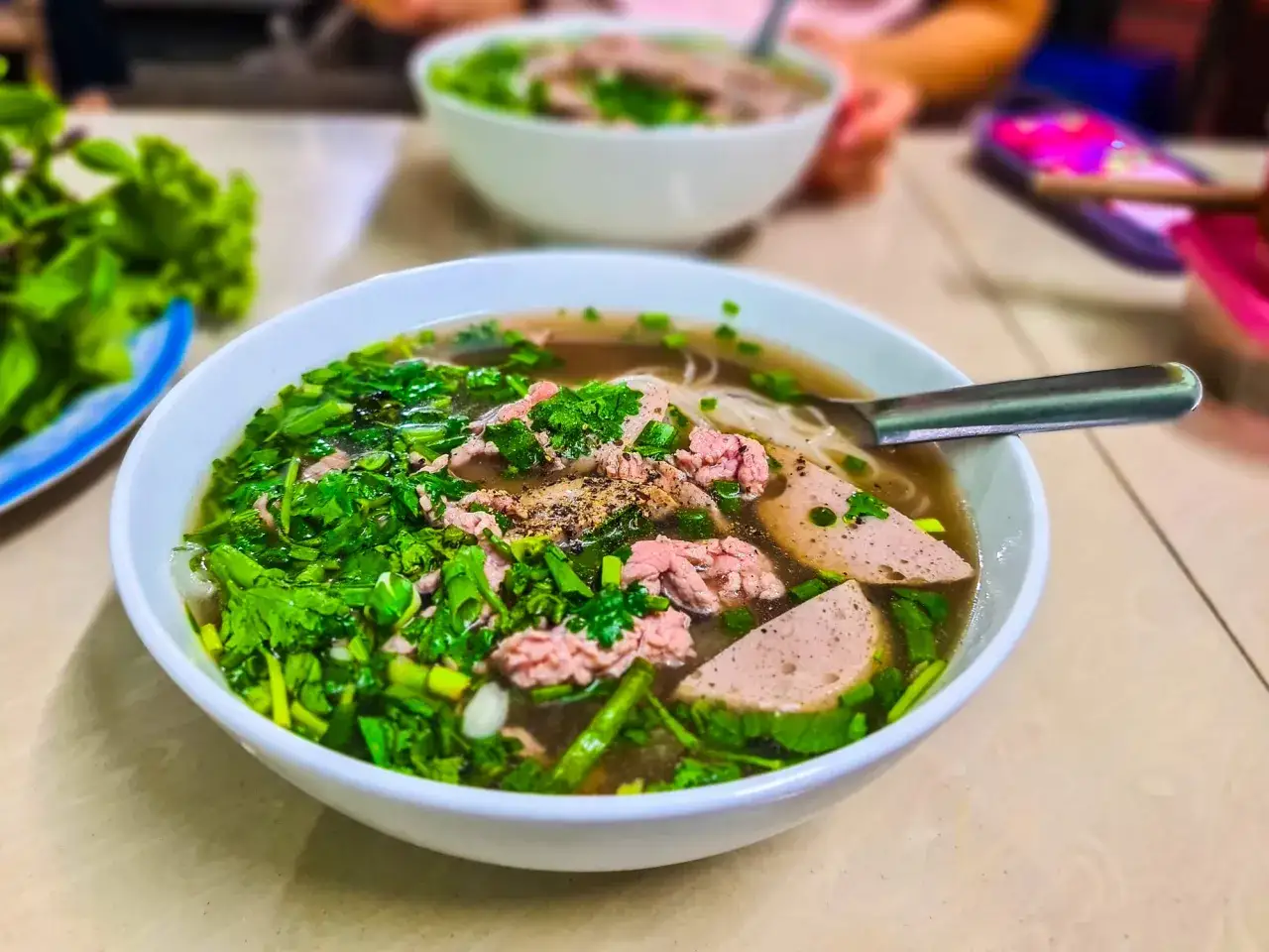 Un bol de soupe pho fumant, garni de fines tranches de b&oelig;uf, de saucisse et d'herbes fra&icirc;ches. Un d&eacute;lice &agrave; savourer.