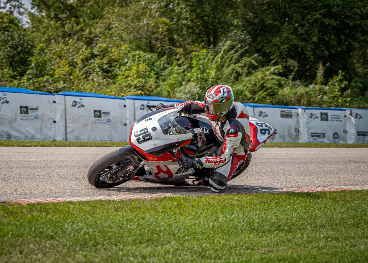 Danny Kent inclinado en una curva cerrada en una carrera de motos, con su traje de cuero rojo y blanco y casco verde.