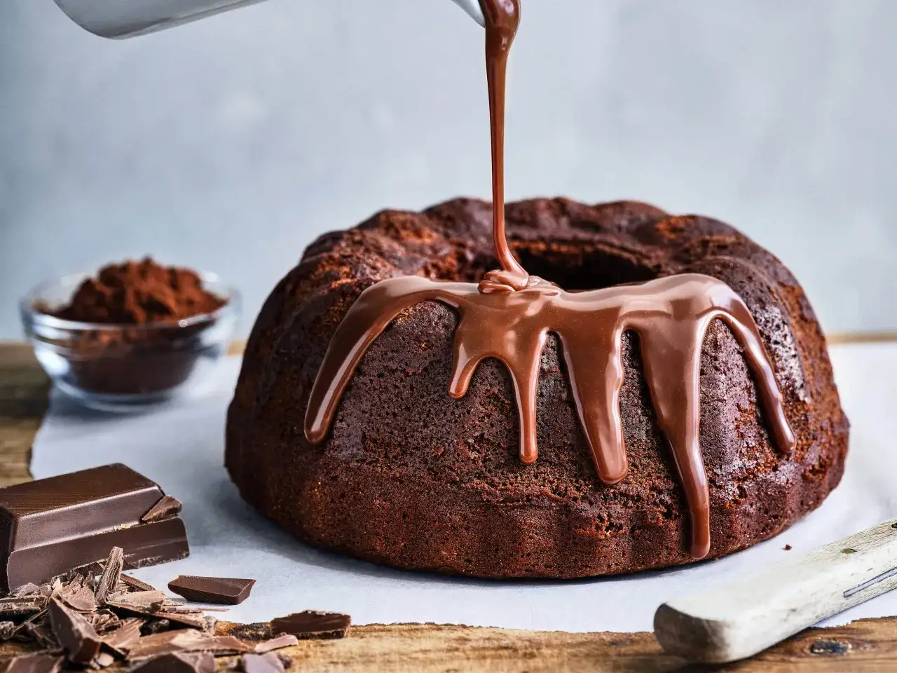 En saftig socker kaka ringlas med chokladglasyr. Bredvid ligger chokladbitar och en sk&aring;l med kakaopulver.