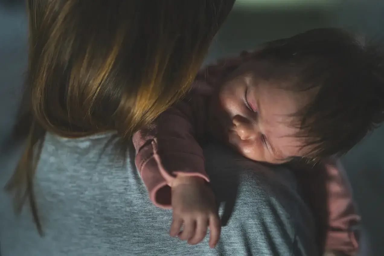 Malutkie dziecko śpi na ramieniu mamy. Choć nie widać płaczu, to właśnie takie chwile, gdy 2 letnie dziecko budzi się w nocy z płaczem, są trudne.