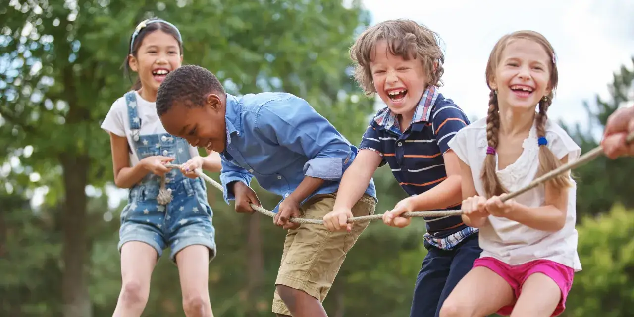 Enfants riant et tirant sur une corde, un exemple joyeux d'éducation populaire en plein air.