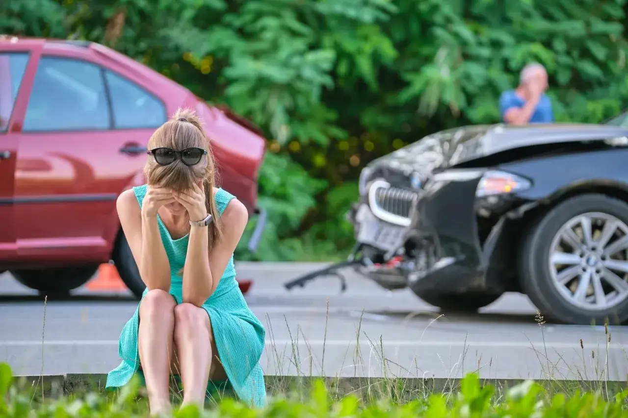 Mujer sentada en el suelo, con las manos en la cara, tras un accidente de coche. Parece que va a soñar con accidente de coche.