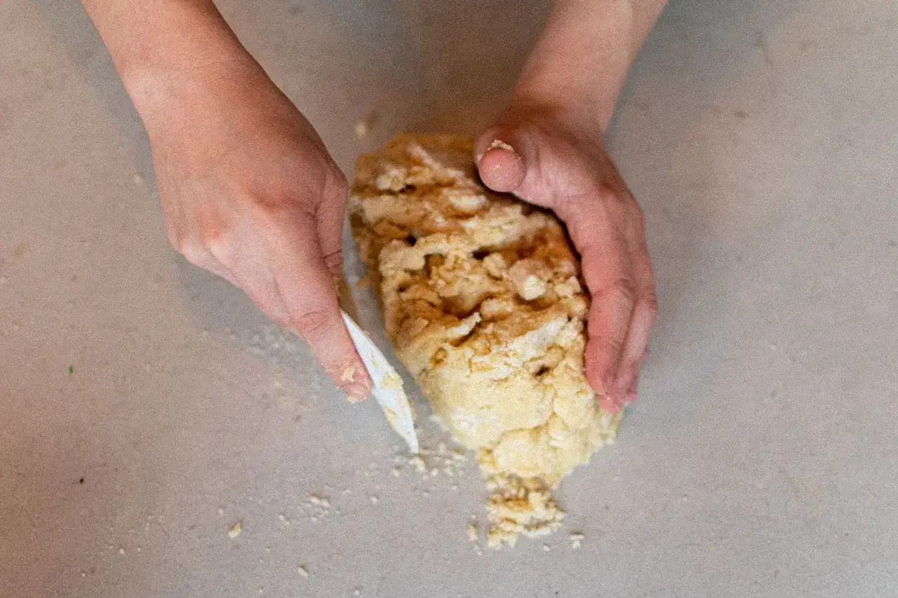 Mains travaillant une pâte sablée friable, avec une spatule pour la rassembler.