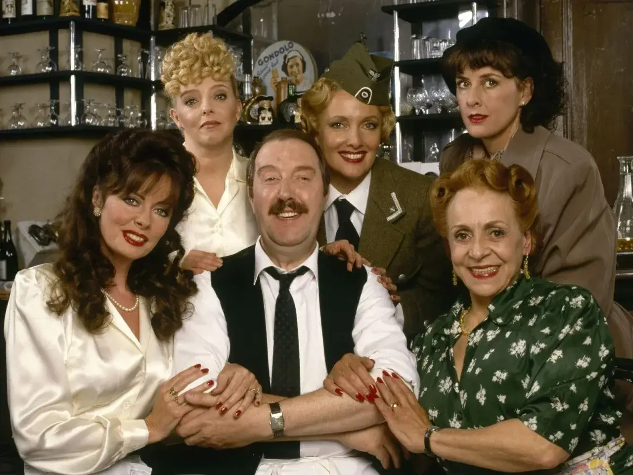 Uśmiechnięta allo allo obsada w kawiarni. René, Michelle, Edith, Yvette, Maria i Leclerc pozują do zdjęcia.