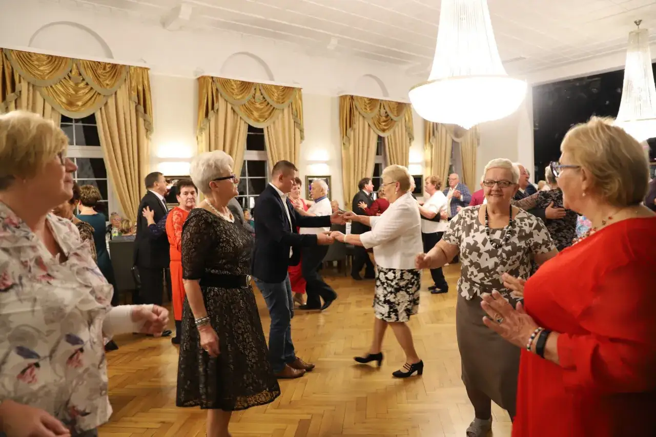 Uczestnicy wieczorków zapoznawczych dla seniorów tańczą w eleganckiej sali.