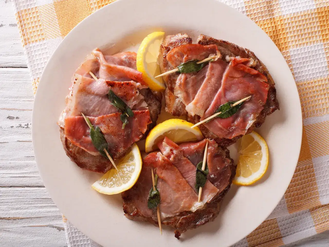 Saltimbocca: Kalbsschnitzel mit Salbei und Parmaschinken, garniert mit Zitronenspalten. Ein Klassiker der italienischen Küche.