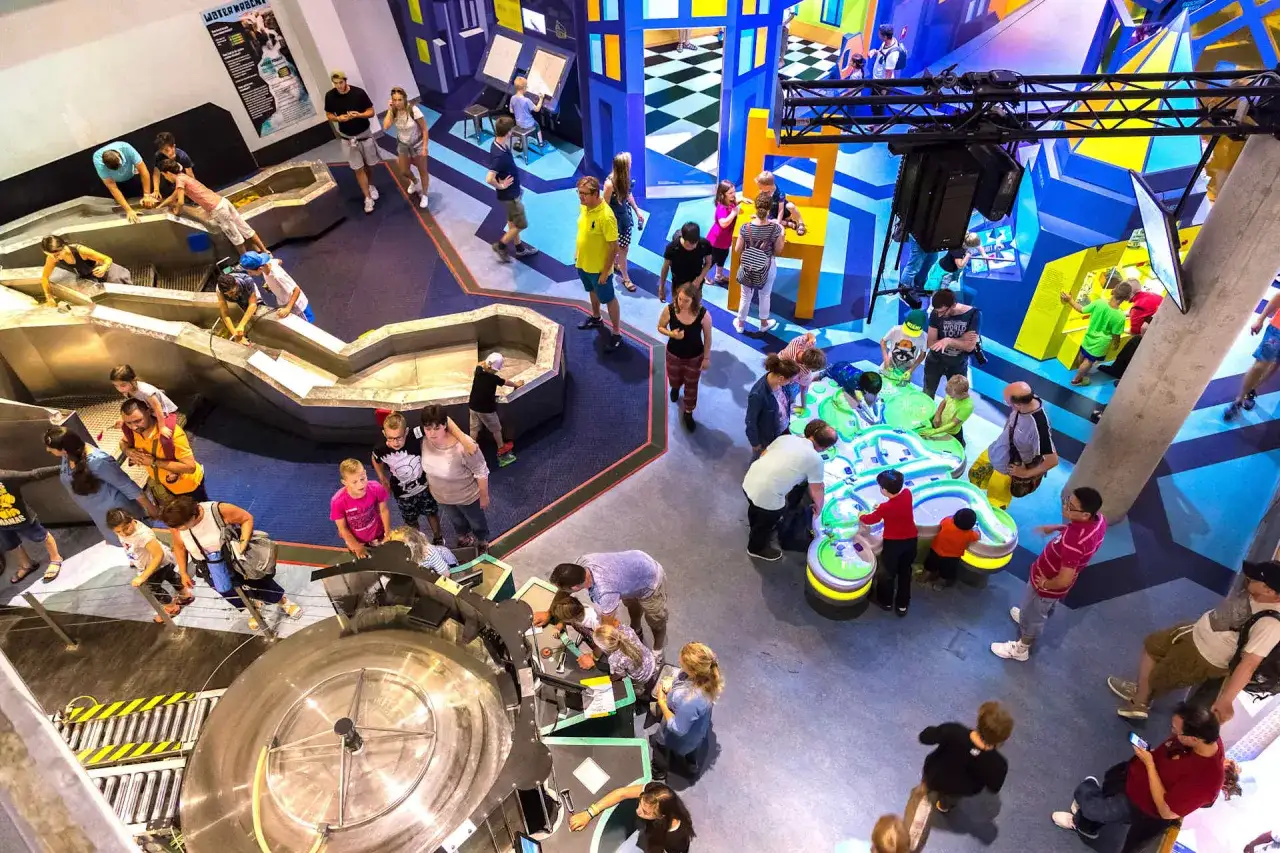 Un grupo de adolescentes y familias exploran un museo interactivo en &Aacute;msterdam, experimentando con exhibiciones de agua y coloridas estructuras.