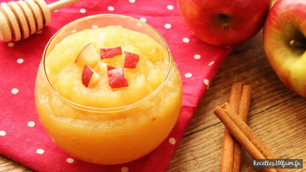 Un verre de compote de pommes maison, garni de d&eacute;s de pommes rouges, sur une serviette &agrave; pois. Des pommes et des b&acirc;tons de cannelle sont &agrave; proximit&eacute;.