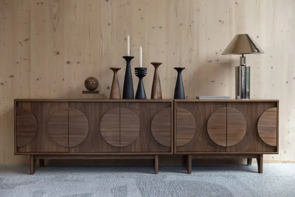 En elegant brun sk&auml;nk med cirkul&auml;ra detaljer. Ljus tr&auml;panel som bakgrund. Vad passar till gr&aring;tt? Kanske dessa m&ouml;rka ljusstakar och en blank lampa.