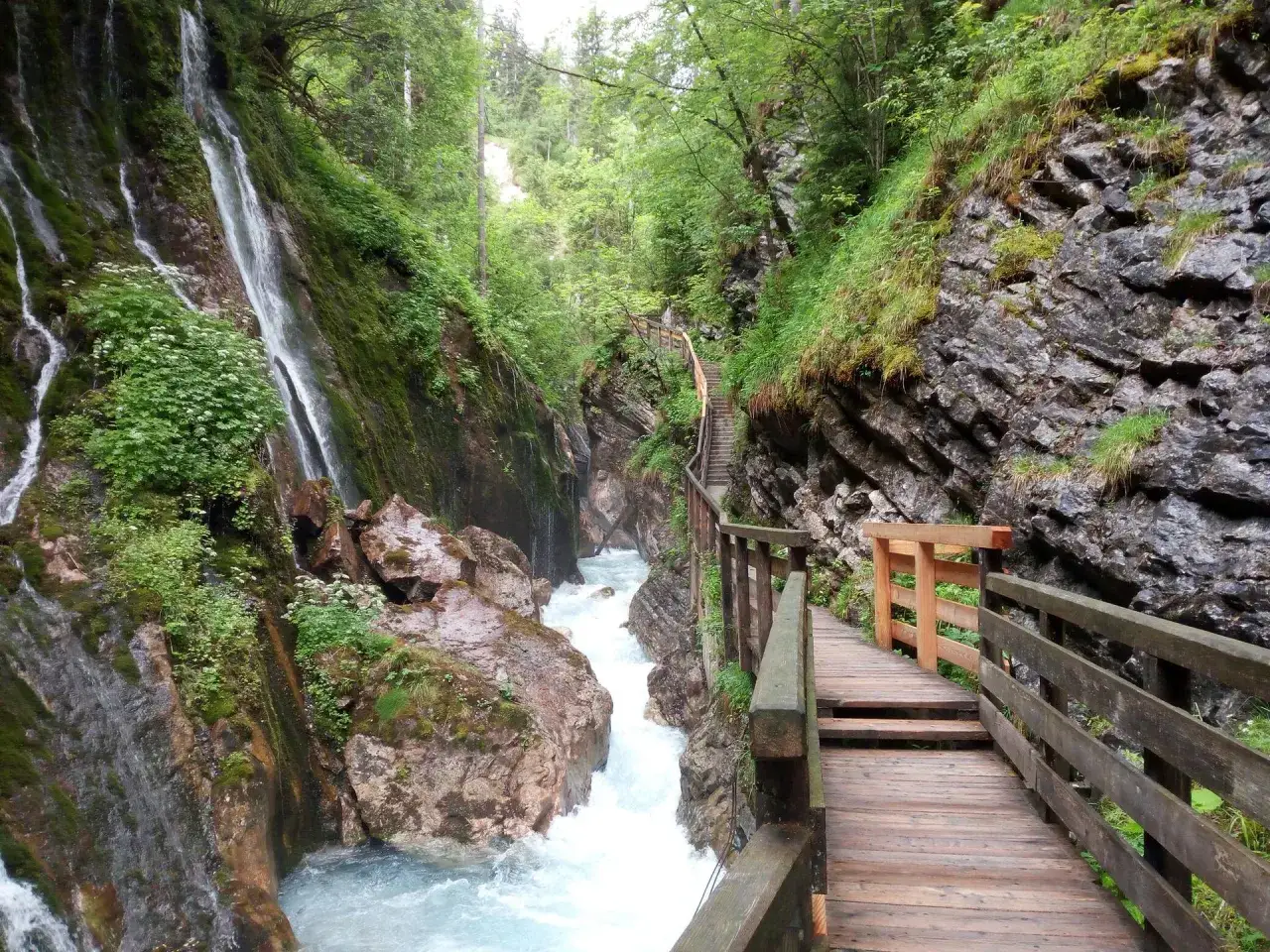 Holzstege f&uuml;hren durch die Klamm Berchtesgaden, vorbei an tosendem Wasser und moosbewachsenen Felsw&auml;nden mit Wasserf&auml;llen.
