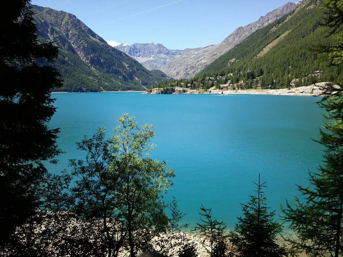 Splendido lago di Ceresole incastonato tra montagne verdi e rocciose, con un cielo azzurro limpido.