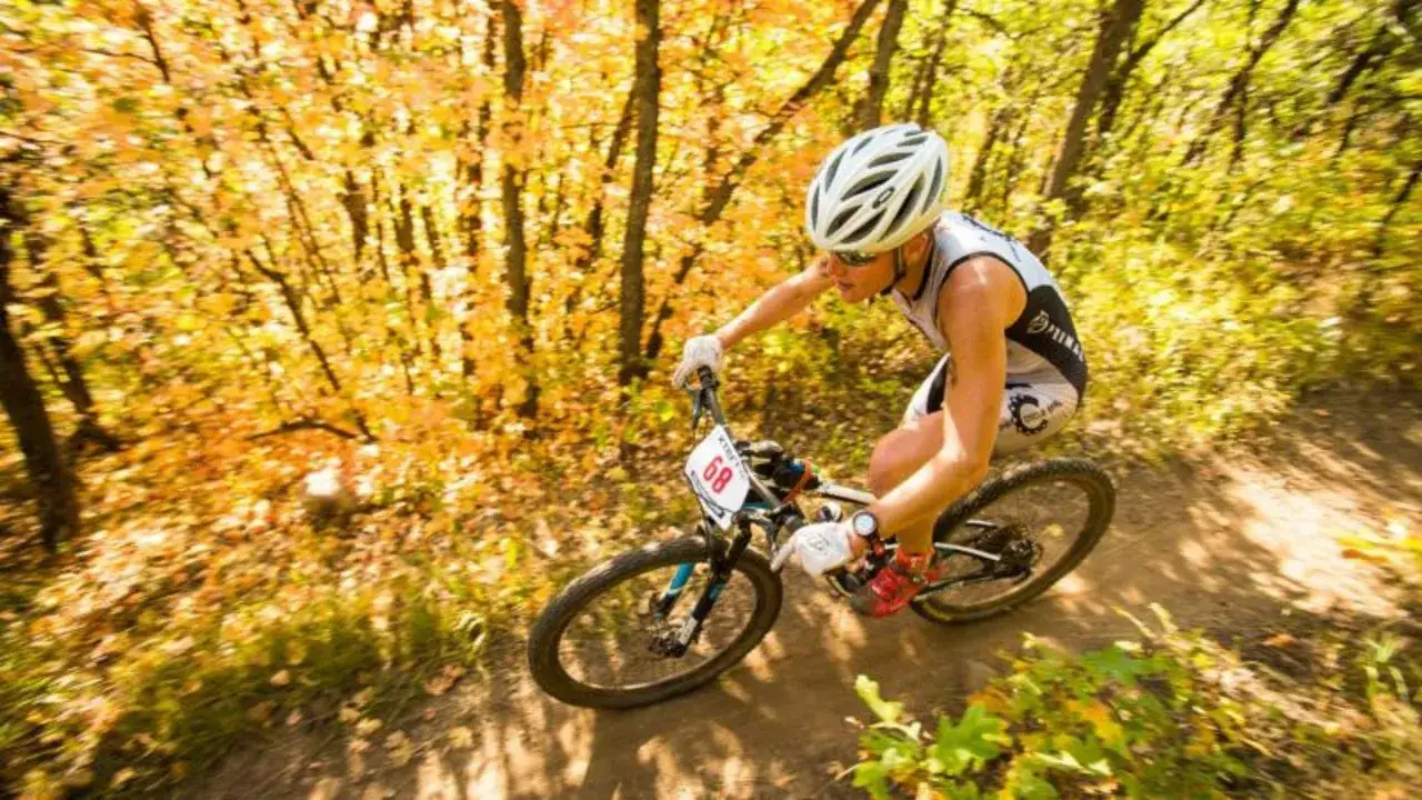 Athlete competes in a mtb triathlon, navigating a wooded trail with vibrant autumn foliage.