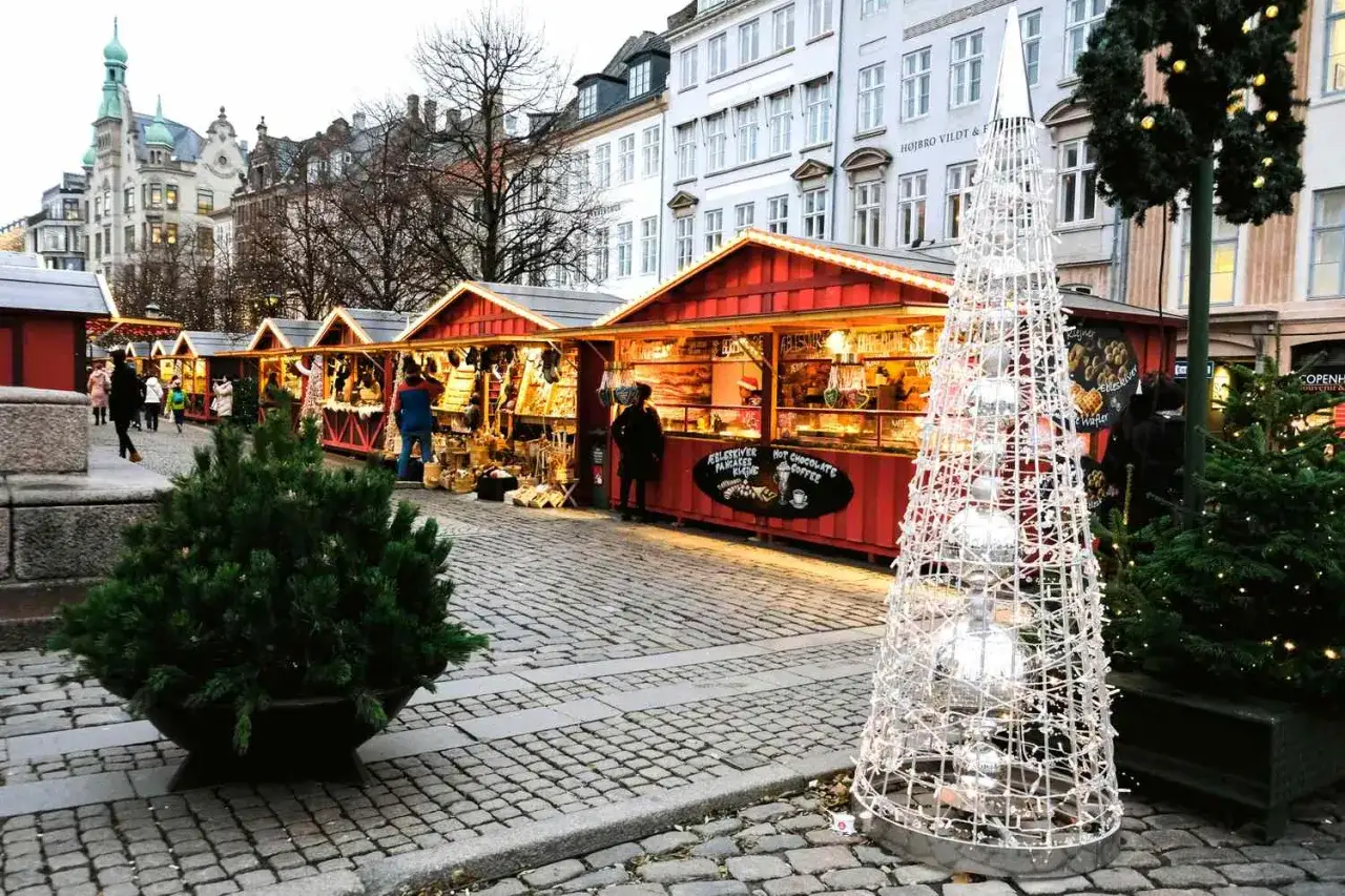 Julmarknad i K&ouml;penhamn, december. R&ouml;da st&aring;nd s&auml;ljer godsaker och hantverk. En stor ljusgran lyser upp torget.