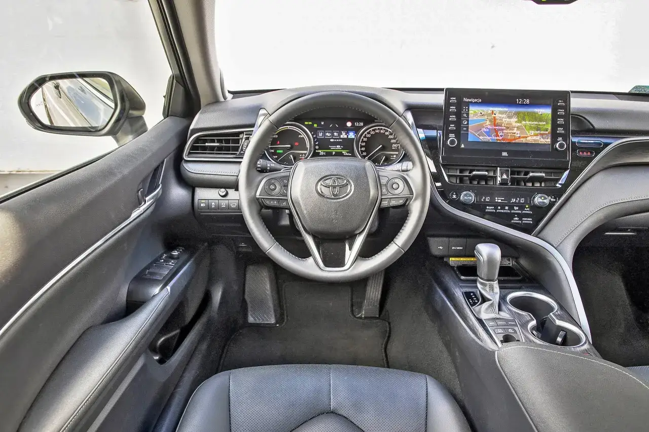 Wnętrze Toyoty Camry 2.5 Hybrid. Kierownica, deska rozdzielcza z nawigacją i panelem klimatyzacji. Dane techniczne dostępne w instrukcji.