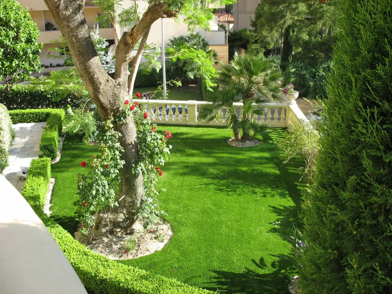 Un jardin luxuriant avec du gazon synth&eacute;tique parfait, id&eacute;al pour savoir comment choisir son gazon synth&eacute;tique. Un arbre imposant et des rosiers ajoutent du charme.