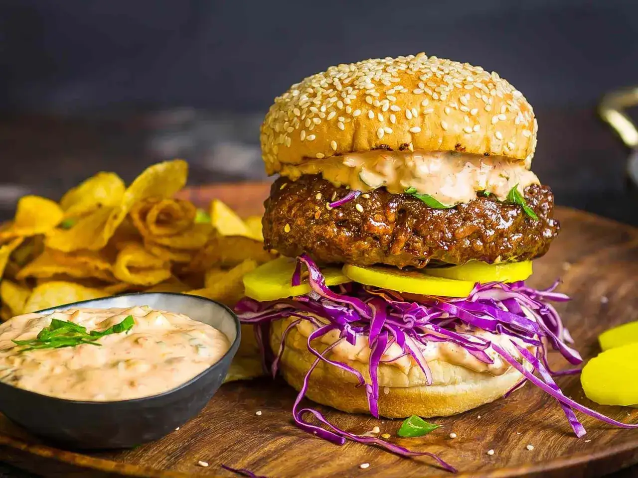 Saftiger korean burger mit Sesambr&ouml;tchen, Rotkohl, Gurken und einer cremigen Sauce, serviert mit knusprigen Chips.
