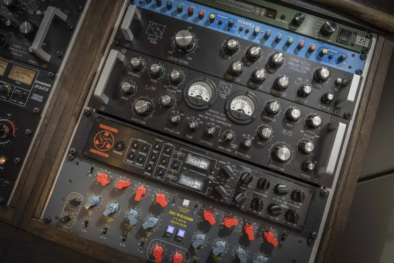 Rack d'équipement audio professionnel pour studio mixage mastering, avec égaliseurs, compresseurs et VU-mètres.