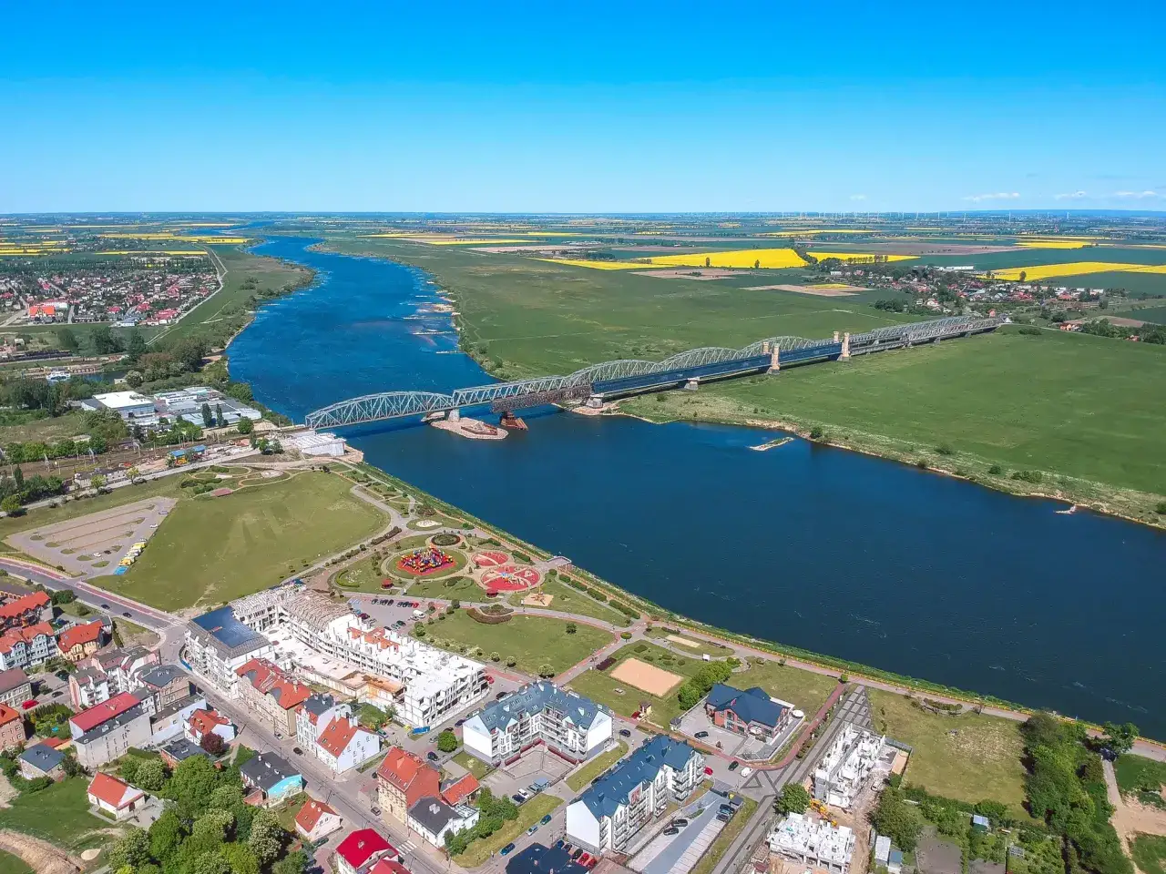 Widok na miasto na Kociewiu z rzeką, mostem i polami rzepaku w tle.