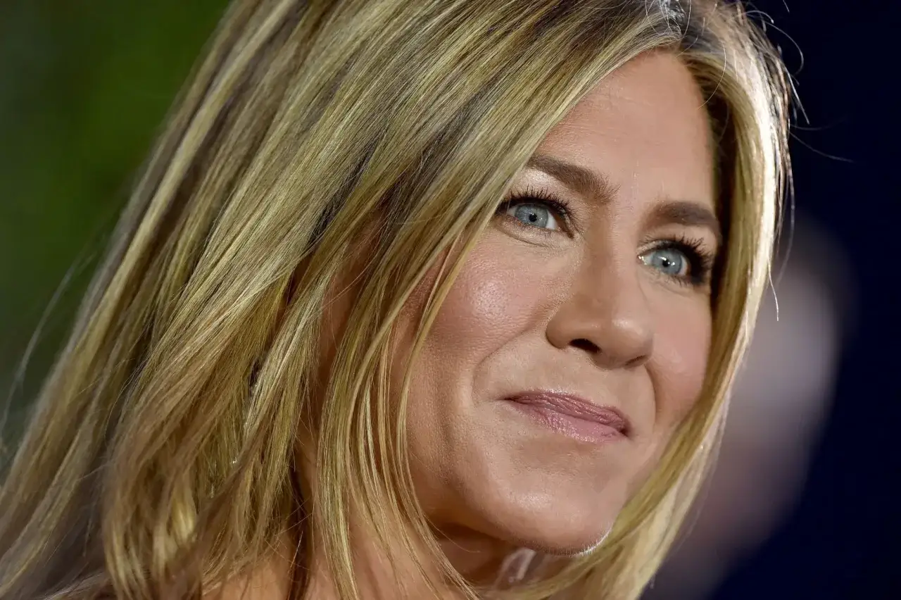 Zbliżenie na twarz Jennifer Aniston, która uśmiecha się. Aktorka, znana z ról, w tym tych, gdzie gra matki, ma blond włosy i niebieskie oczy.