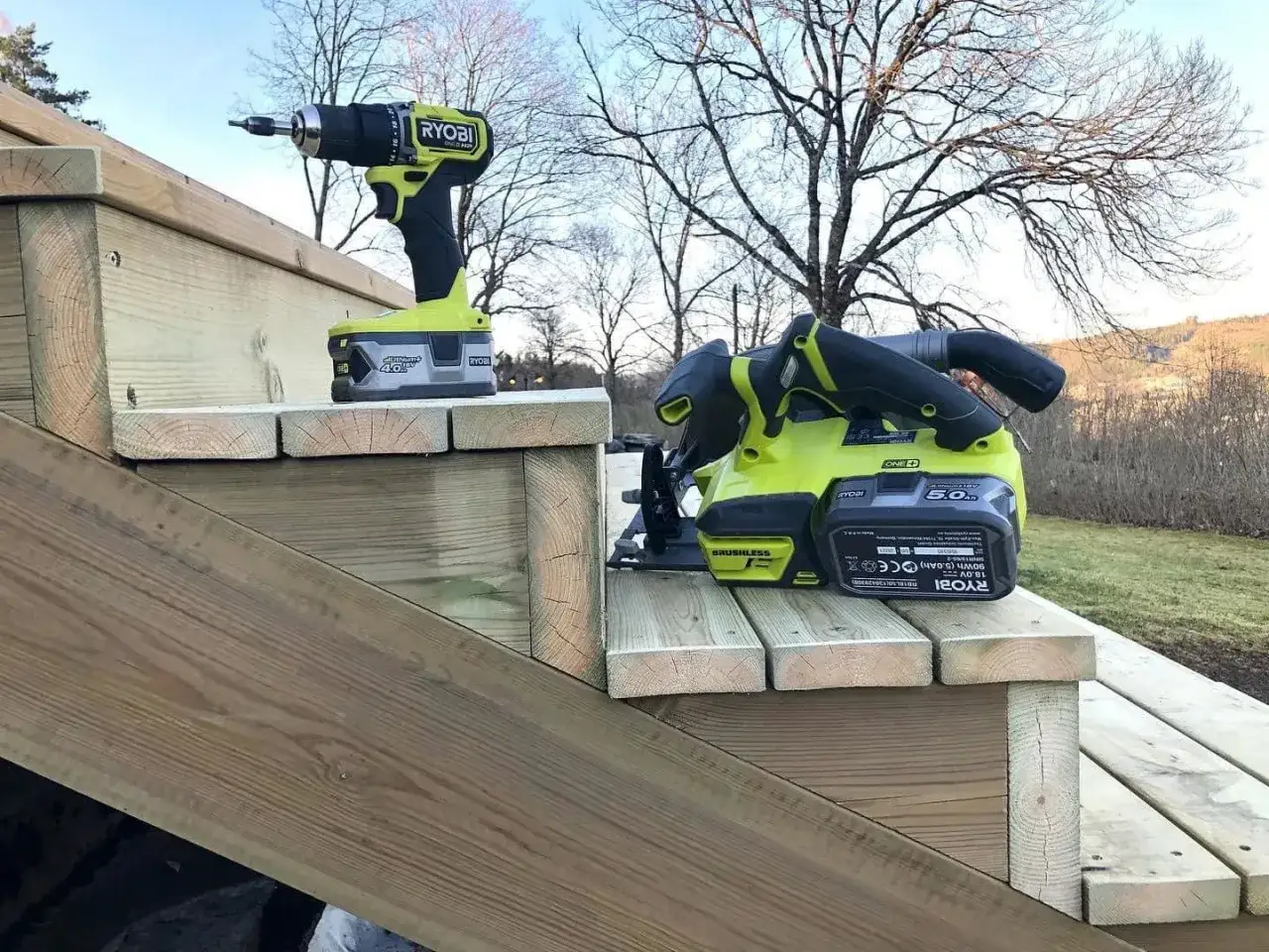 Ryobi-verktyg redo att bygga vangstycke till en ny trappa. En skruvdragare och en cirkelsåg står på trätrappstegen.