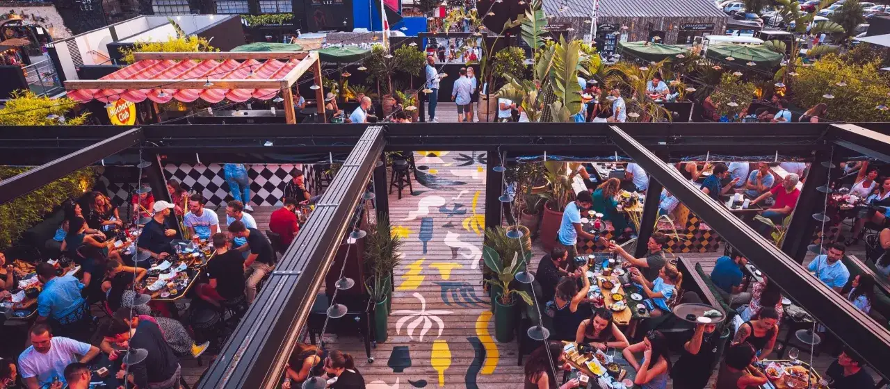 Gente disfrutando en una terraza con decoración que evoca cosas típicas de Francia, como banderas y toldos a rayas.