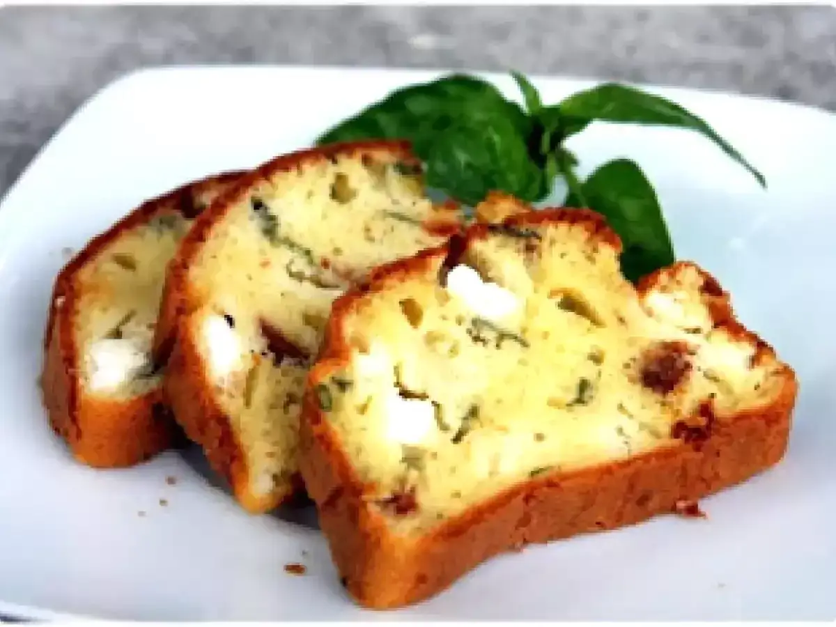 Tranches d'un cake savoureux aux tomates séchées et feta, garni de feuilles de basilic frais.