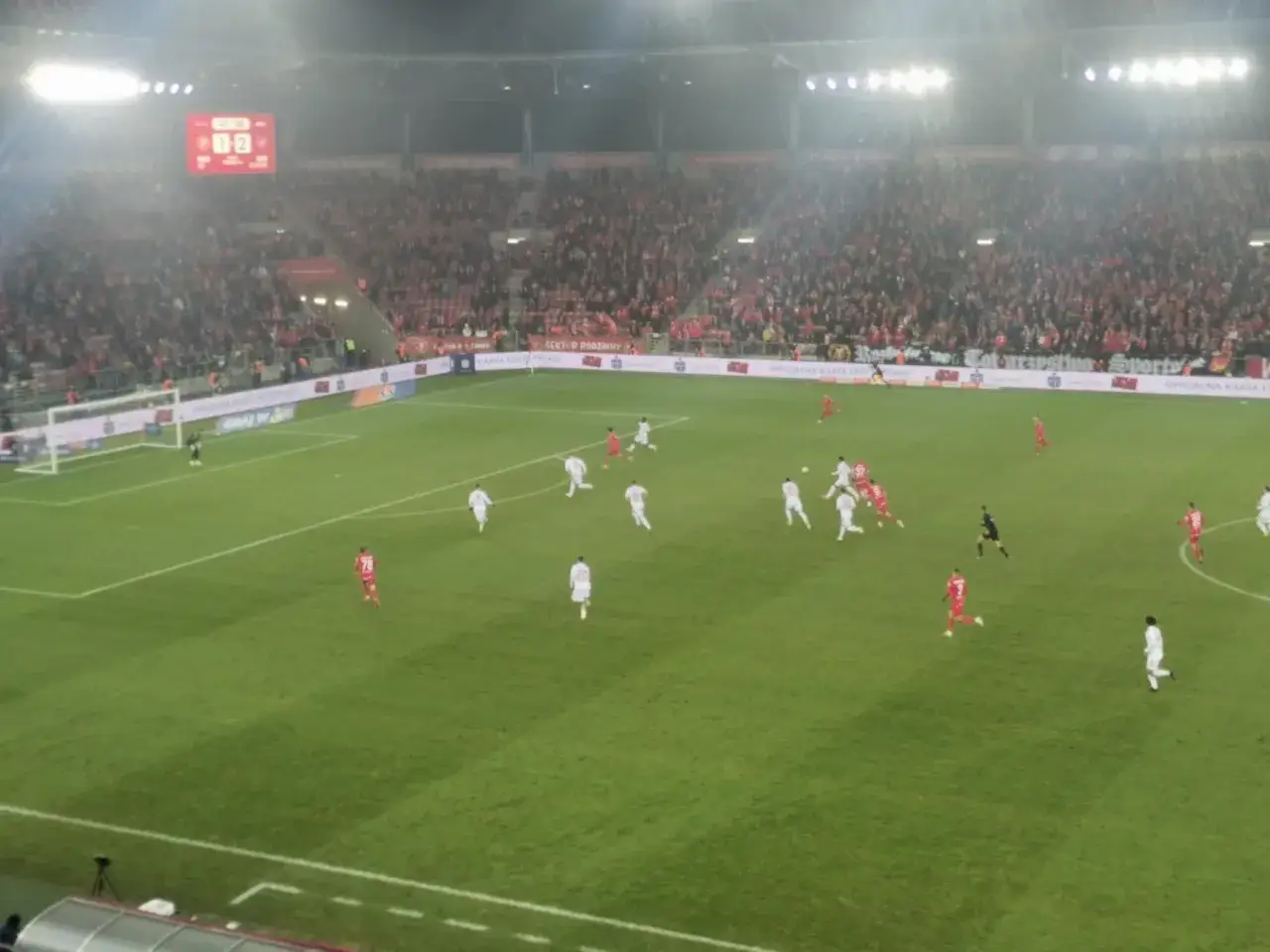 Mecz Raków Częstochowa – Widzew Łódź. Piłkarze w białych strojach atakują bramkę, trybuny wypełnione kibicami. Wynik 1:2.