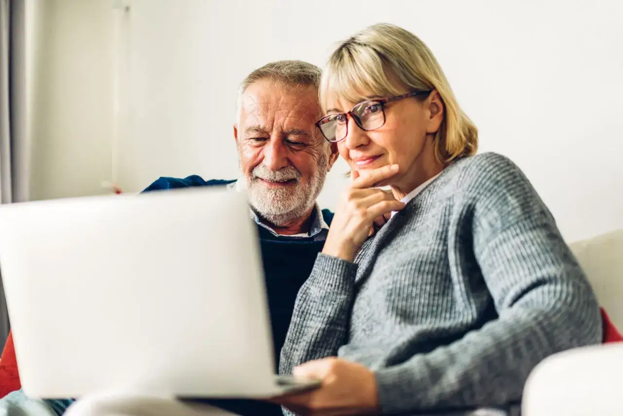 Couple âgé consultant un ordinateur, peut-être pour le calcul du paiement maison de retraite par les descendants.