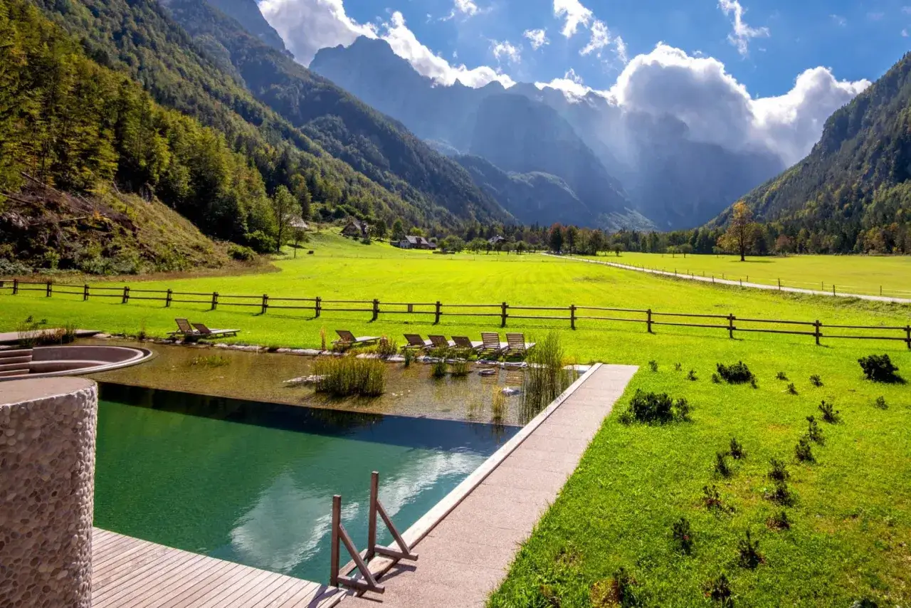 Piscine naturelle dans un paysage alpin, conforme à l'esprit de l'article R.111-19 du code de l'urbanisme. Chaises longues sur l'herbe.