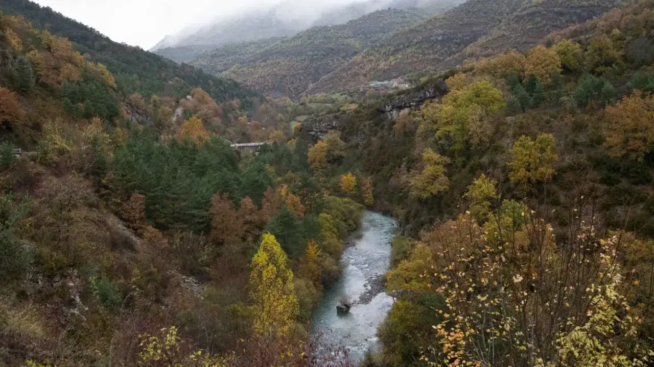 El **valle de Ansó** se despliega con un río serpenteante entre montañas cubiertas de bosques otoñales en tonos ocres y verdes.