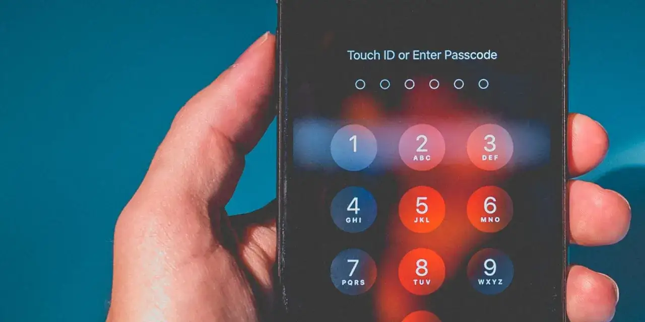 Dłoń z palcami na ekranie iPhone'a, pokazująca klawiaturę numeryczną. Dowiedz się, jak odblokować iPhone'a.