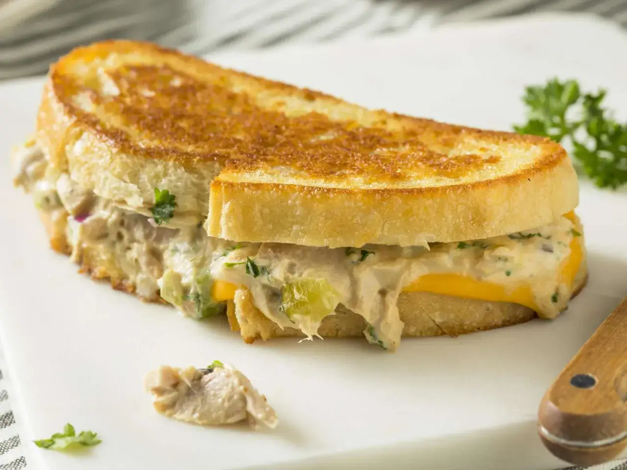 Ein goldbraun geröstetes Tuna Melt Sandwich mit geschmolzenem Käse und einer Füllung aus Thunfischsalat, garniert mit Petersilie.