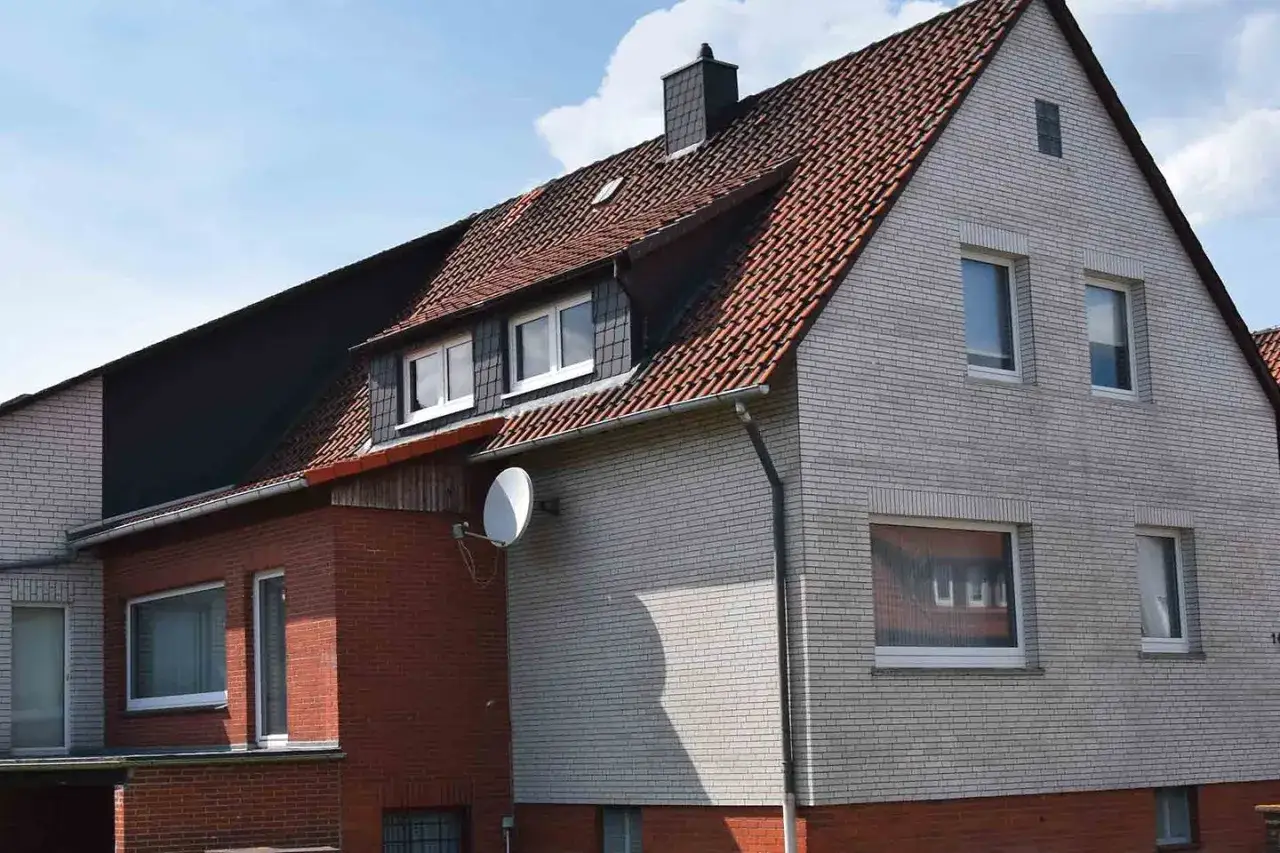 Haus mit rotem Ziegeldach und heller Klinkerfassade. Satellitenschüssel montiert. Die **Sanierungspflicht** scheint hier vor dem Aus zu stehen, da das Gebäude renovierungsbedürftig wirkt.
