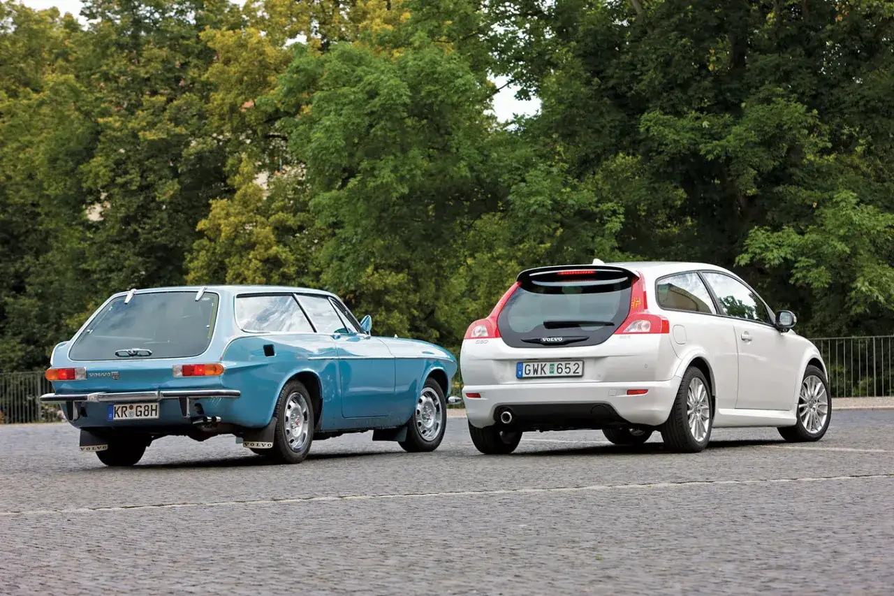 Niebieskie Volvo P1800 ES i białe Volvo C30 stoją obok siebie, prezentując ewolucję designu marki.
