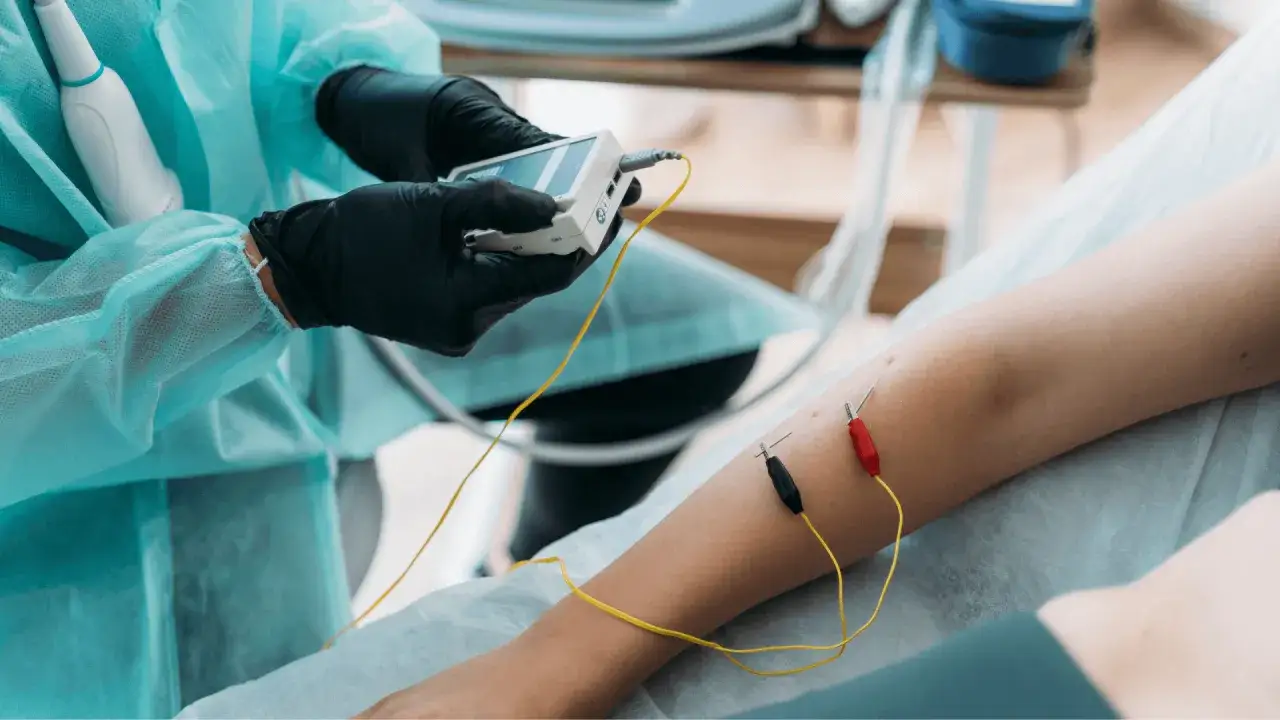 Lekarz w rękawiczkach podłącza elektrody do nogi pacjenta, by leczyć rwę udową.