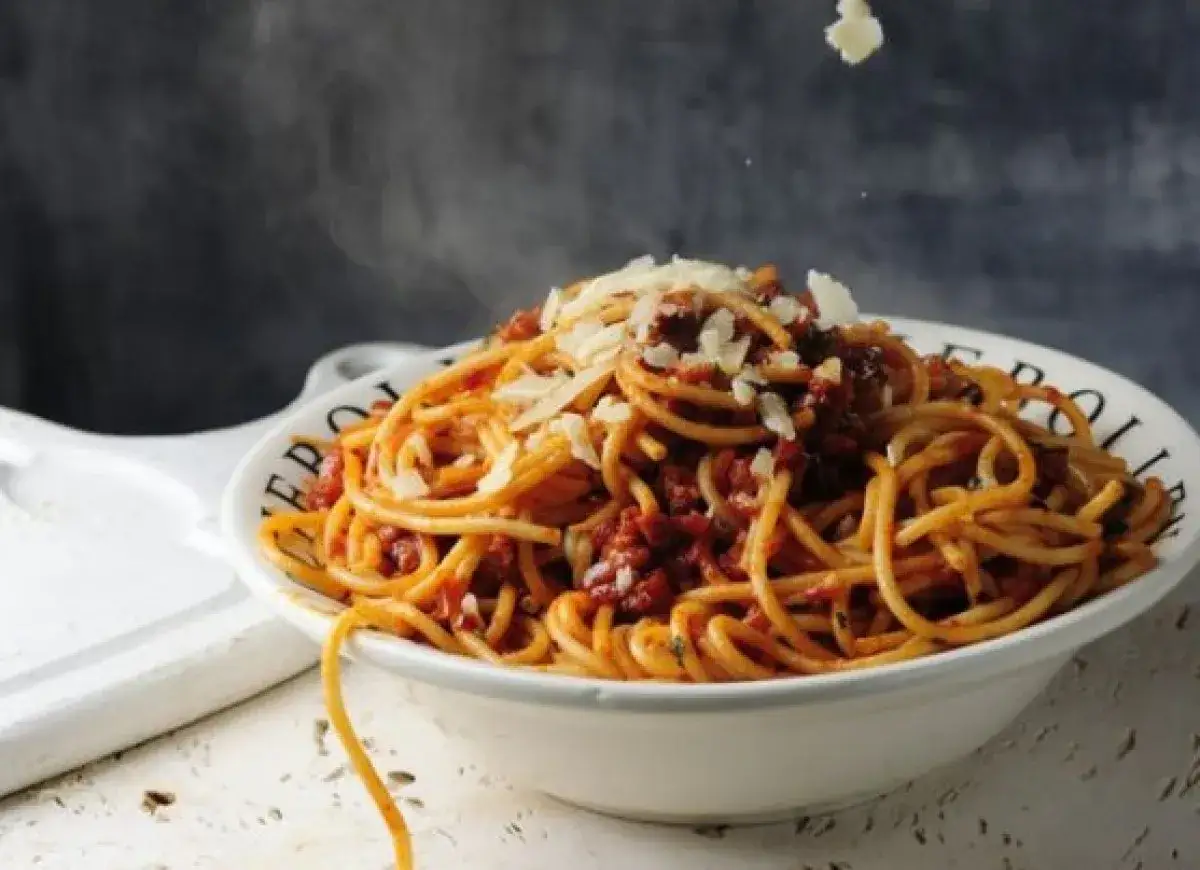 Gorący makaron bucatini z sosem bolońskim i parmezanem, unosząca się para dodaje apetycznego wyglądu.