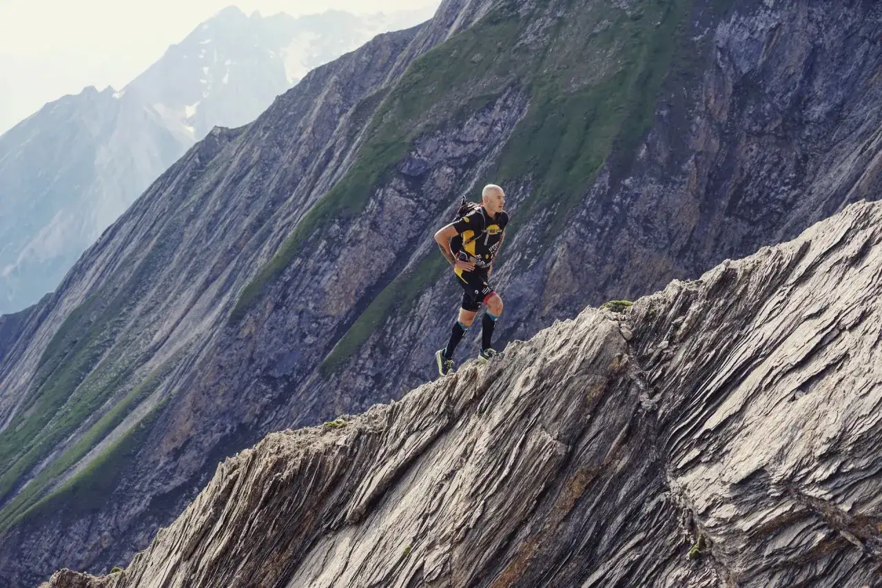 Un coureur en tenue de sport, le visage concentr&eacute;, gravit un sentier escarp&eacute; et fractionn&eacute; en cote. Le paysage montagneux est spectaculaire.