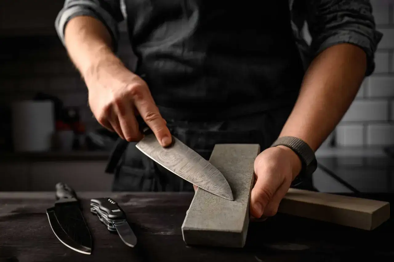 Chef afila un cuchillo de damasco sobre una piedra de afilar. Aprende como afilar cuchillos con afilador para mantenerlos perfectos.